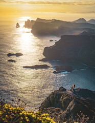 Female tourist sits at beautiful viewpoint on steep cliff overlooking the sea and the rugged...