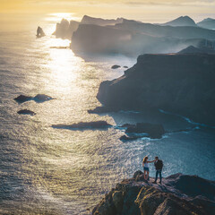 Tourist kisses his girlfriend's hand at viewpoint on steep cliff overlooking the sea and rugged...