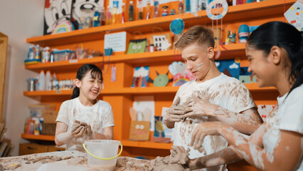 Smart caucasian teenager and happy friend with mixed races put clay on body in art lesson. Diverse highschool student playing and modeling cup of clay at workshop in creative activity. Edification.