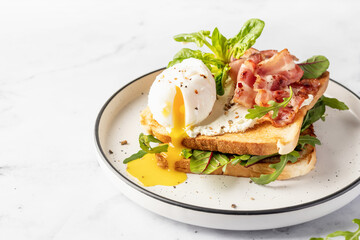 Toasts sandwich with poached egg, arugula, bacon and cream cheese on white plate marble background