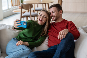 Happy positive couple with gladden face expression doing selfie shot on cellphone, smiling into...