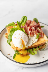 Toasts sandwich with poached egg, arugula, bacon and cream cheese on white plate marble background