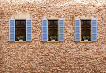 Symmetry in Stonework: Trio of Blue Shutters on a Textured Wall