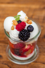 Frozen yoghurt with summer fruit in a glass on a wooden table in a restaurant