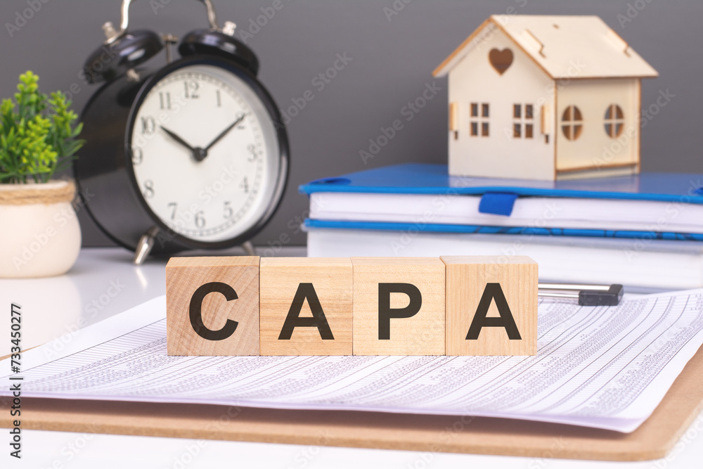 Poster 'capa' on wooden blocks, with a small house and alarm clock, conveys implementing corrective actions