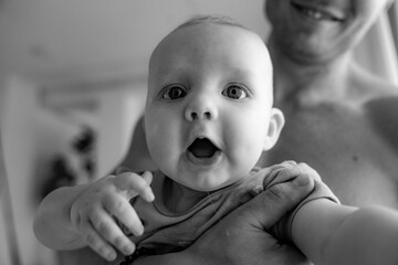 Baby looks up at the camera with big smile while his father holds him in this photograph by London...