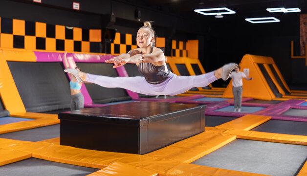 Dynamic Middle-aged Woman Wearing Sport Clothes High Jumping In Trampoline Arena