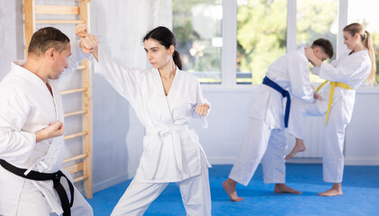 Adult man and young woman karatekas train karate in group in studio..