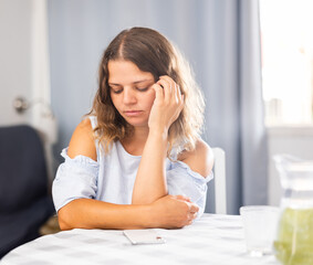 Upset young girl sitting at the table in her room