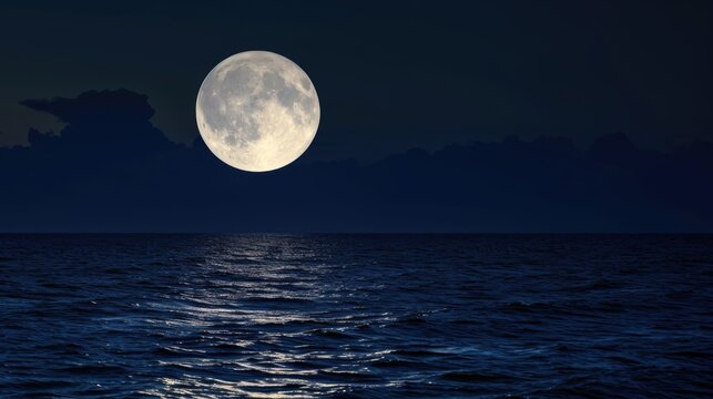 A full moon rising over a body of water. © tilialucida