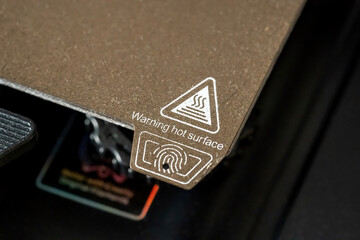 A 3D printer heated bed building pad hot surface warning label seen from up close, nobody. 3D printing equipment and accessories simple concept, device usage instructions warning icons symbols detail