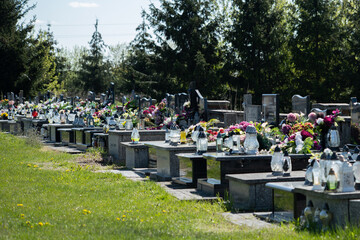 Row of graves in a small city town cemetery, simple generic Eastern European graveyard. Cemetery grounds, graves with flowers and votive lights, burial place, Poland, All Saints Day concept, nobody