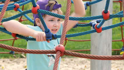 Young elementary school age girl wearing a baseball cap playing on the playground, climbing, portrait, face closeup, slow motion Real people lifestyle, kid playing, looking at camera, outdoor activity