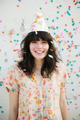 A girl's joy radiates as she dons a party hat, adding a playful touch to her fashionable ensemble against the backdrop of a wall