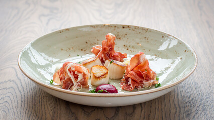 Fried scallops with ham on a plate on wooden table