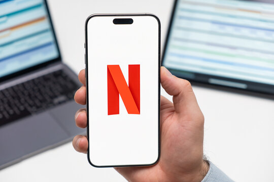 PRAGUE, CZECH REPUBLIC - JANUARY 21 2024: Netflix logo on the screen of a cell phone in mans hand and laptop on the background. 