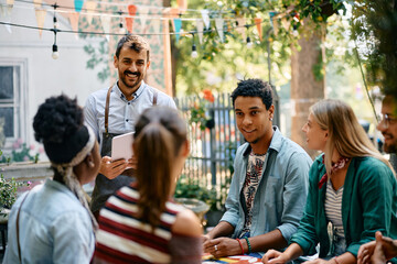 Happy waiter serving multiracial group of friends in cafe.