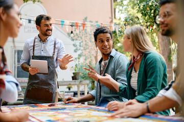 Multiracial group of happy friends talking to waiter in cafe.