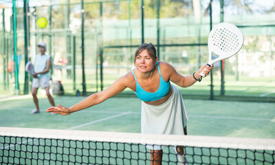 Sporty young woman playing padel on open court on summer day, ready to hit ball with left-handed...