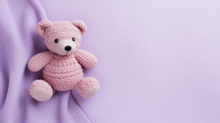 A small knitted amigurumi bear toy on a purple blanket, on a purple background. Flat lay, top view, copy space. space for text