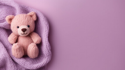 Fototapeta premium A small knitted amigurumi bear toy on a violet blanket, on a violet background. Flat lay, top view, copy space. space for text