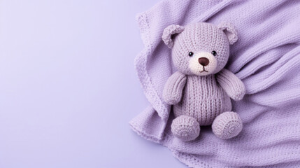 A small knitted amigurumi bear toy on a violet blanket, on a violet background. Flat lay, top view, copy space. space for text