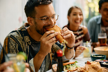 Young man enjoying in taste of tacos while having lunch with friends in restaurant.