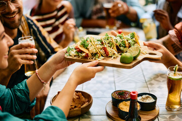 Close up of friends having tacos while gathering for lunch in restaurant.