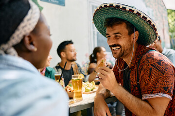 Cheerful man eating nacho chips and drinking beer while gathering with his friends.