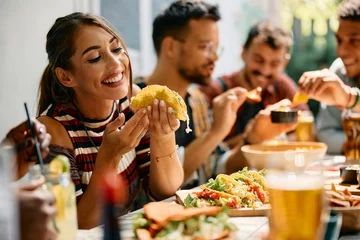 Schilderijen op glas Happy woman eating tacos during lunch with friends in Mexican restaurant. © Drazen