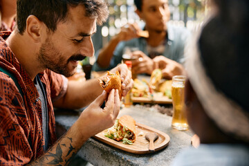 Smiling man eating tacos while being with friends in restaurant.