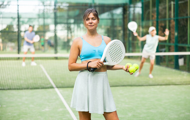 Positive girl looking at camera while playing padel at court outdoor