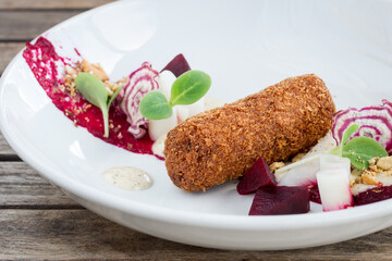 Close up of shrimp croquette appetizer with vegetables on white plate on wooden table in restaurant