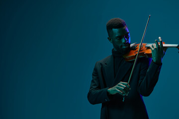 Elegant musician in black suit playing melodious violin against vibrant blue background, artistic...