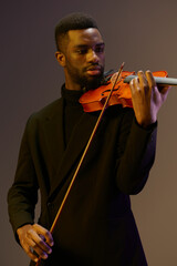 Elegant musician in black suit playing violin on gray background in classic musical performance...
