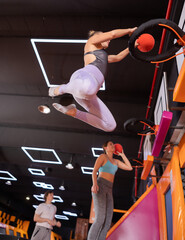 Fototapeta na wymiar Active European female in sportswear playing basketball while bouncing on colorful trampolines indoors in leisure sports center