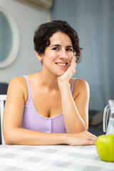 Portrait of positive woman sitting at a table in her apartment room