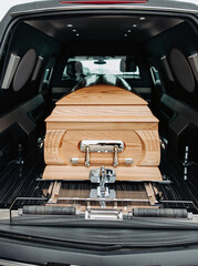 A wooden coffin stands in a black hearse. A simple wooden coffin in a black car. Funeral and...