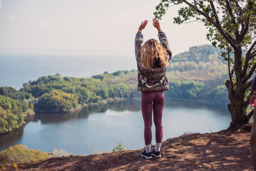 Beautiful young woman standing in front of wonderful lake with her hands up, enjoying the mindful...