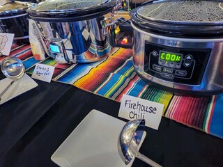 Row of crockpots on colorful striped cloth for a chili cookoff contest