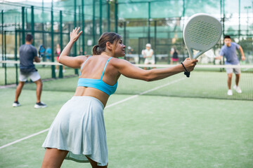 Attractive woman padel tennis player training on court. Rear view of young woman using racket to hit ball.