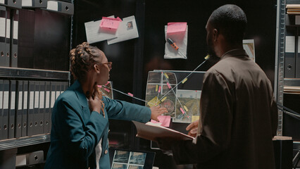 Detective partners analyzing criminal records in office, looking at archive photos. Police...