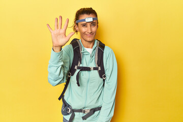 Mountain gear and frontal light on yellow smiling cheerful showing number five with fingers.