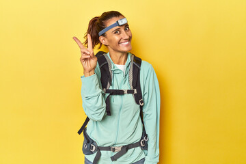 Mountain gear and frontal light on yellow joyful and carefree showing a peace symbol with fingers.