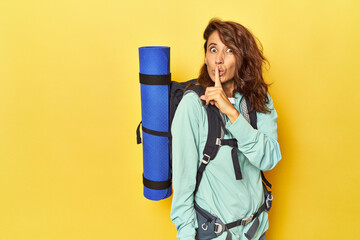 Woman with hiking backpack and mat on yellow keeping a secret or asking for silence.