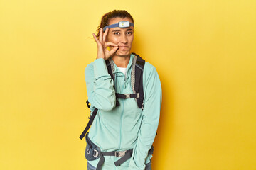 Mountain gear and frontal light on yellow with fingers on lips keeping a secret.