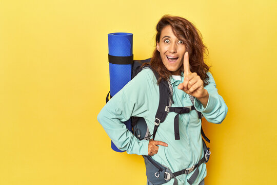 Woman with hiking backpack and mat on yellow having an idea, inspiration concept.