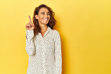 Middle-aged woman on a yellow backdrop showing number one with finger.