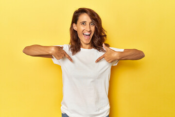 Middle-aged woman on a yellow backdrop surprised pointing with finger, smiling broadly.