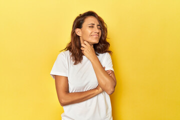 Middle-aged woman on a yellow backdrop suffers pain in throat due a virus or infection.
